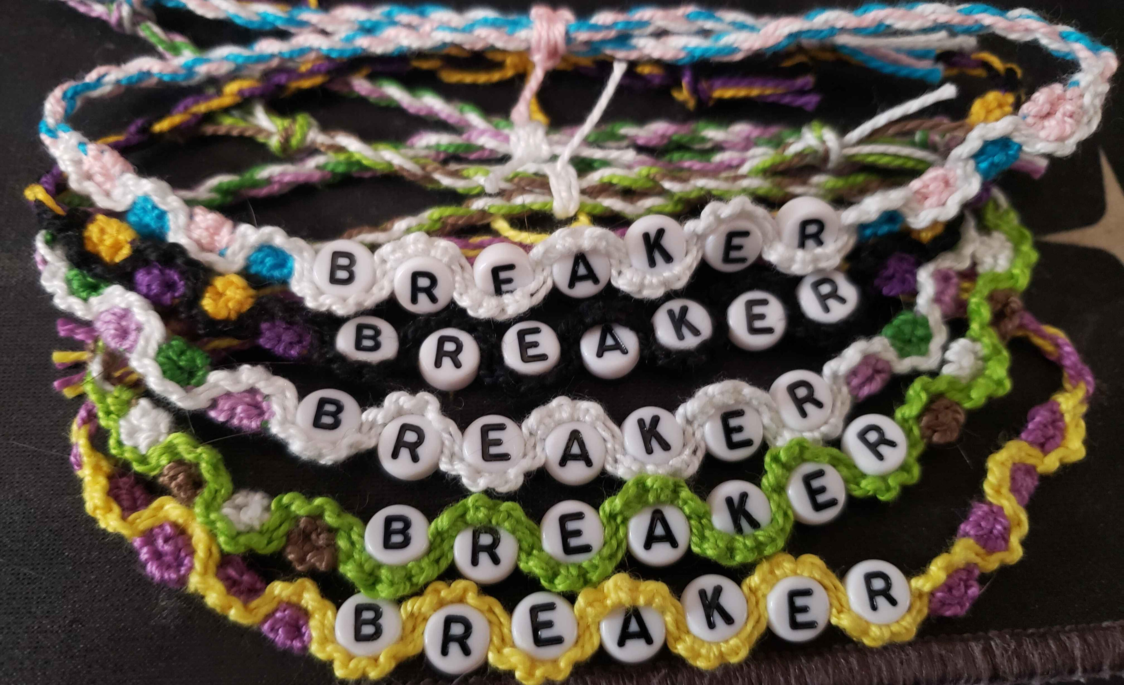 Friendship bracelets that say BREAKER. They are made in several colors, each representing a different pride flag.